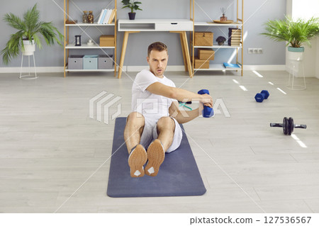 Concentrated athletic man doing exercises with dumbbells during sports training at home. Concentrated athletic man doing exercises with dumbbells during sports training at home. 127536567