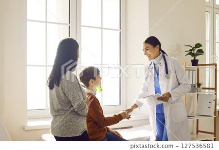 Portrait of a little boy patient with his mother talking with paediatrician doctor in clinic. 127536581