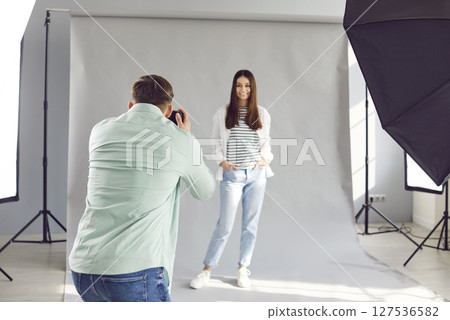 Back view of young man photographer shooting female model in photo studio with light equipment. Back view of young man photographer shooting female model in photo studio with light equipment. 127536582