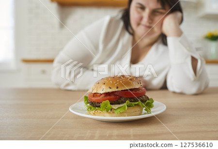 Overweight woman looking at burger lying in front of her Overweight woman looking at burger lying in front of her 127536610