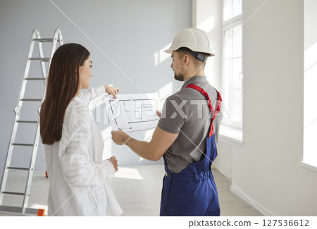 Foreman showing to a homeowner woman blueprint with design project of her new apartment. 127536612