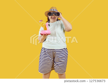 Fat woman in hat and sunglasses holding cocktail showing thumb up sign on yellow background. 127536673