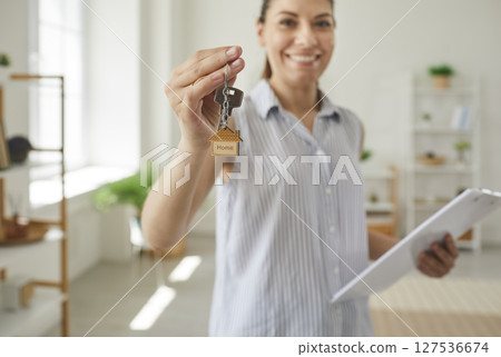 Happy woman real estate agent with clipboard gives you key to new house or apartment Happy woman real estate agent with clipboard gives you key to new house or apartment 127536674