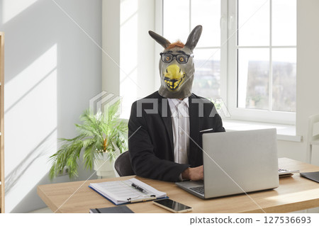 Businessman in donkey head mask using laptop computer in office Businessman in donkey head mask using laptop computer in office 127536693