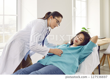 Gynecologist doctor examining heartbeat in the abdomen of pregnant woman with stethoscope. 127536697