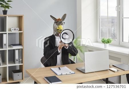 Funny man wearing donkey animal mask sitting at the desk in office and shouting in mouthpiece Funny man wearing donkey animal mask sitting at the desk in office and shouting in mouthpiece 127536701