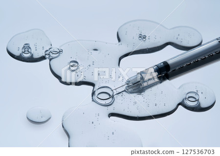 The texture of a cosmetic preparation and a syringe for injection on a blue background. The texture of a cosmetic preparation and a syringe for injection on a blue background. 127536703