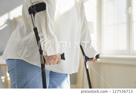 Cropped photo of a handicapped overweight fat woman with crutches trying to walk at home. Cropped photo of a handicapped overweight fat woman with crutches trying to walk at home. 127536713