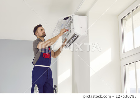 Young man repairing air conditioner standing on stepladder Young man repairing air conditioner standing on stepladder 127536785
