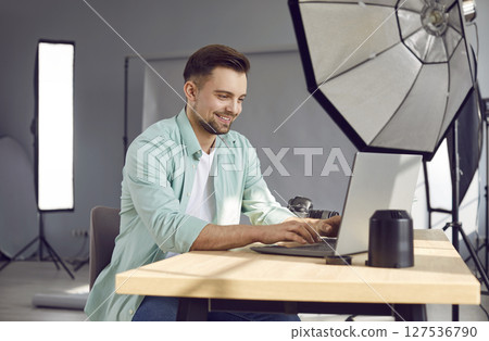 Smiling male professional photographer using laptop in photo studio 127536790