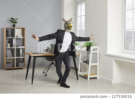 Joyful funny business man in a donkey animal mask having fun and dancing in the office. Joyful funny business man in a donkey animal mask having fun and dancing in the office. 127536818