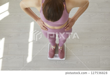 Thin young woman stands on floor scale, measuring kilograms after morning sports workout. Thin young woman stands on floor scale, measuring kilograms after morning sports workout. 127536828