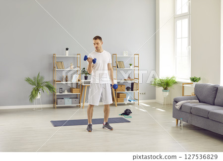 Ordinary man in morning in his home performs sports training and pumps his arm muscles. 127536829