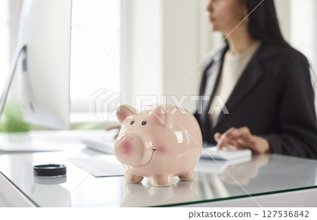 Piggy bank on office table, woman investing money, planning future, manage finances to save money Piggy bank on office table, woman investing money, planning future, manage finances to save money 127536842