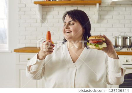 Overweight woman chooses between carrot and hamburger and decides in favor of healthy food 127536844