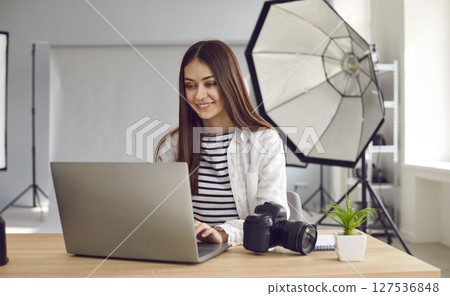 Smiling woman photographer retouching photo on laptop in production studio. Smiling woman photographer retouching photo on laptop in production studio. 127536848