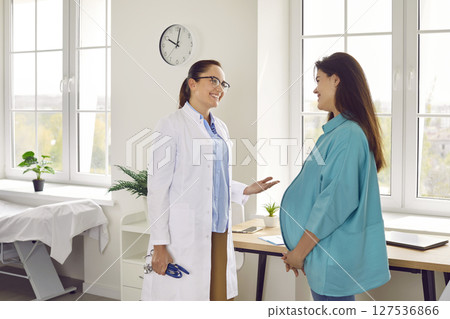 Happy pregnant woman talking with her gynecologist doctor during medical exam in clinic. 127536866