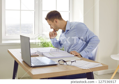 Prtrait of a young businessman looking through paper documents and working at office. 127536917