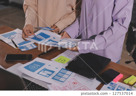 Close up ux developer and ui designer brainstorming about mobile app interface wireframe design on table with customer breif and color code at modern office.Creative digital development agency. 127537014