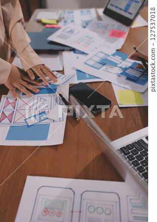Close up ux developer and ui designer brainstorming about mobile app interface wireframe design on table with customer breif and color code at modern office.Creative digital development agency. 127537018