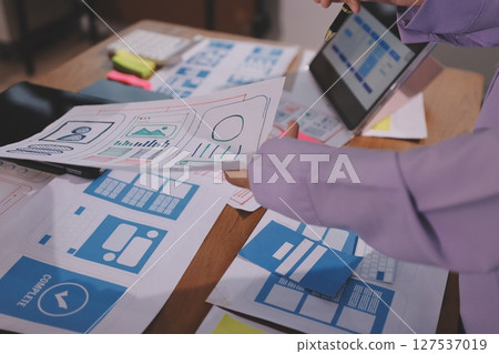 Close up ux developer and ui designer brainstorming about mobile app interface wireframe design on table with customer breif and color code at modern office.Creative digital development agency. Close up ux developer and ui designer brainstorming about mobile app interface wireframe design on table with customer breif and color code at modern office.Creative digital development agency. 127537019