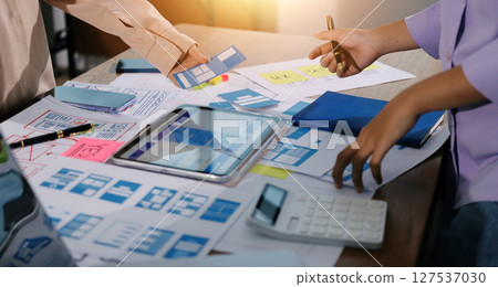 Close up ux developer and ui designer brainstorming about mobile app interface wireframe design on table with customer breif and color code at modern office.Creative digital development agency. Close up ux developer and ui designer brainstorming about mobile app interface wireframe design on table with customer breif and color code at modern office.Creative digital development agency. 127537030