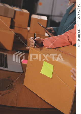 Startup SME small business entrepreneur of freelance Asian woman wearing apron using laptop and box to receive and review orders online to prepare to pack sell to customers, online sme business ideas. Startup SME small business entrepreneur of freelance Asian woman wearing apron using laptop and box to receive and review orders online to prepare to pack sell to customers, online sme business ideas. 127537039