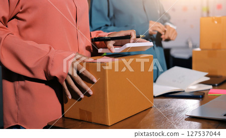 Startup SME small business entrepreneur of freelance Asian woman wearing apron using laptop and box to receive and review orders online to prepare to pack sell to customers, online sme business ideas. 127537044