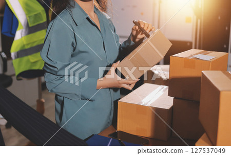 Startup SME small business entrepreneur of freelance Asian woman wearing apron using laptop and box to receive and review orders online to prepare to pack sell to customers, online sme business ideas. 127537049