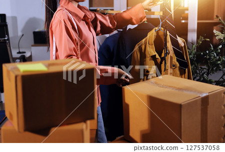 Startup SME small business entrepreneur of freelance Asian woman wearing apron using laptop and box to receive and review orders online to prepare to pack sell to customers, online sme business ideas. Startup SME small business entrepreneur of freelance Asian woman wearing apron using laptop and box to receive and review orders online to prepare to pack sell to customers, online sme business ideas. 127537058