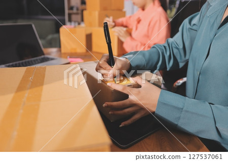 Startup SME small business entrepreneur of freelance Asian woman wearing apron using laptop and box to receive and review orders online to prepare to pack sell to customers, online sme business ideas. 127537061