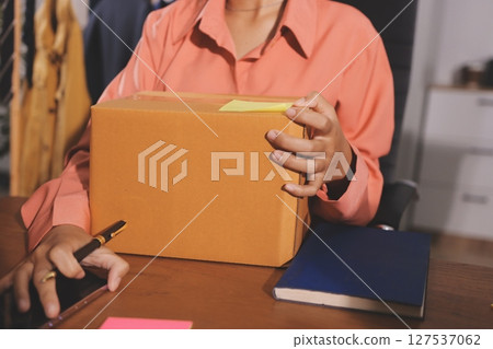 Startup SME small business entrepreneur of freelance Asian woman wearing apron using laptop and box to receive and review orders online to prepare to pack sell to customers, online sme business ideas. 127537062