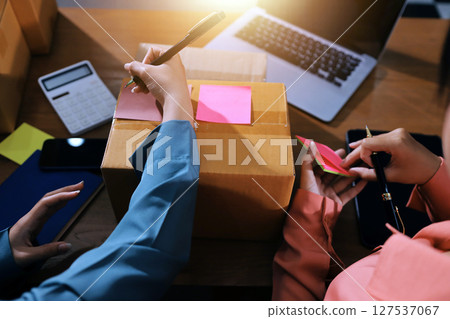 Startup SME small business entrepreneur of freelance Asian woman wearing apron using laptop and box to receive and review orders online to prepare to pack sell to customers, online sme business ideas. 127537067
