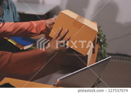 Startup SME small business entrepreneur of freelance Asian woman wearing apron using laptop and box to receive and review orders online to prepare to pack sell to customers, online sme business ideas. Startup SME small business entrepreneur of freelance Asian woman wearing apron using laptop and box to receive and review orders online to prepare to pack sell to customers, online sme business ideas. 127537074