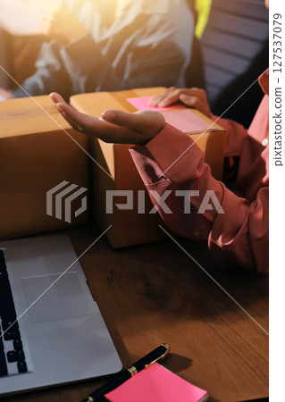 Startup SME small business entrepreneur of freelance Asian woman wearing apron using laptop and box to receive and review orders online to prepare to pack sell to customers, online sme business ideas. 127537079