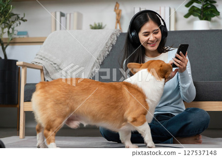 Pet Interaction and Digital Connection. Woman smiling while using smartphone as her dog approaches. 127537148
