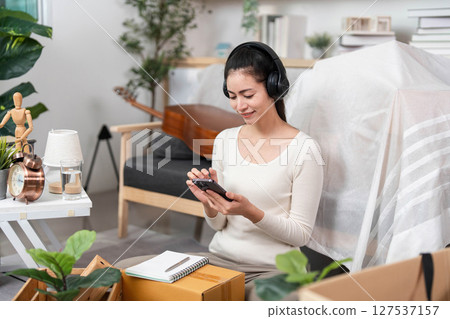 Moving and Relaxing. Woman using smartphone while sitting on the floor during packing. 127537157