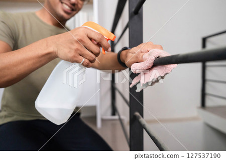 Home Cleaning and Maintenance. A man actively cleaning a railing with a spray bottle and cloth. 127537190