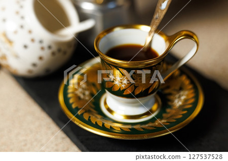 Elegant coffee cup adorned with golden details sits on a decorative saucer amidst a cozy cafe atmosphere 127537528