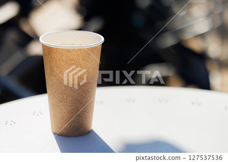 Coffee held in a textured cup on a sunlit table, capturing the essence of a relaxing outdoor moment 127537536