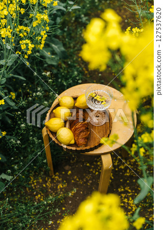 Fresh fruits and pastries on a table in a vibrant yellow flower field during springtime Fresh fruits and pastries on a table in a vibrant yellow flower field during springtime 127537620