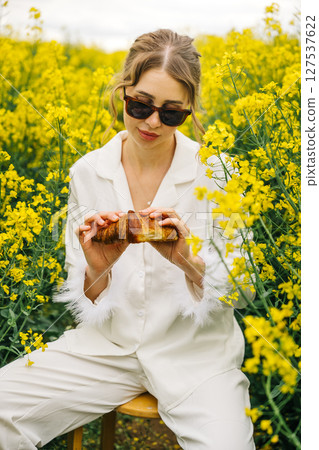 Woman enjoying a croissant in a yellow flower field during daytime Woman enjoying a croissant in a yellow flower field during daytime 127537622