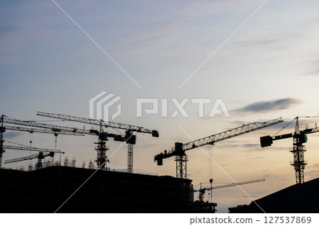 Construction cranes silhouetted against a cloudy sky 127537869