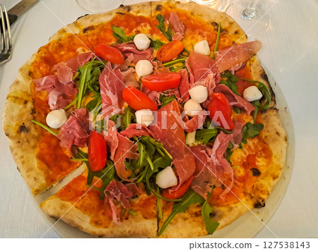 Delicious round pizza with prosciutto, mozzarella, cherry tomatoes, arugula. Top view 127538143