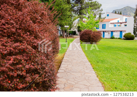 Peaceful walkway through a Mediterranean hotel garden. Summer vacation, leisure strolls and nature-filled resort experience. 127538213