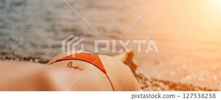 A woman sunbathes on the beach, lying on her stomach in a red swimsuit against the sea backdrop. A woman sunbathes on the beach, lying on her stomach in a red swimsuit against the sea backdrop. 127538238