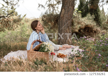 Picnic basket nature: Woman enjoys serene daytime picnic near trees for relaxation/outdoor dining. Picnic basket nature: Woman enjoys serene daytime picnic near trees for relaxation/outdoor dining. 127538261