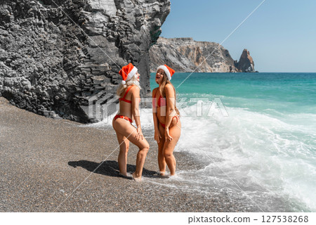 Women in Santa Claus hats run into the sea dressed in red swimsuits. Celebrating the New Year in a hot country Women in Santa Claus hats run into the sea dressed in red swimsuits. Celebrating the New Year in a hot country 127538268