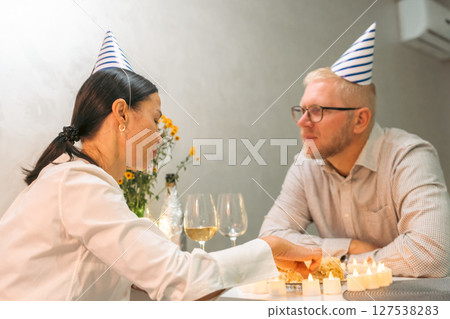 Birthday Couple Celebration: Indoor party scene; man woman wearing hats; intimate moment sharing cake. 127538283