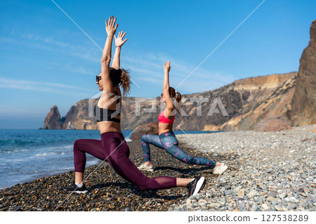 Yoga Beach Fitness: Women stretch in warrior pose at sunny shoreline for health, against rocks. 127538289